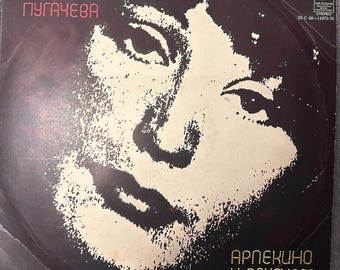 Op de afbeelding: Een vierkante vinylplatenhoes met een zwart-wit portret met hoog contrast van een persoon. De tekst luidt "АЛЛА ПУГАЧЕВА" linksboven en "АРЛЕКИНО И ДРУГИЕ" rechtsonder, vergezeld door kleine iconen van theatermaskers.