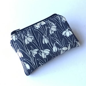 May include: A navy blue zippered pouch with a white floral pattern featuring snowdrop flowers. The pouch is rectangular and made of fabric. The zipper is black.