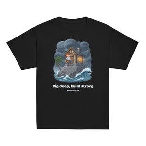 Op de afbeelding: Een zwart t-shirt met een afbeelding van een persoon voor een huis op een rots tijdens een storm. De tekst luidt: Dig deep, build strong, Matthew 7:24. De illustratie bevat donkere wolken, beukende oceaangolven en een palmboom.