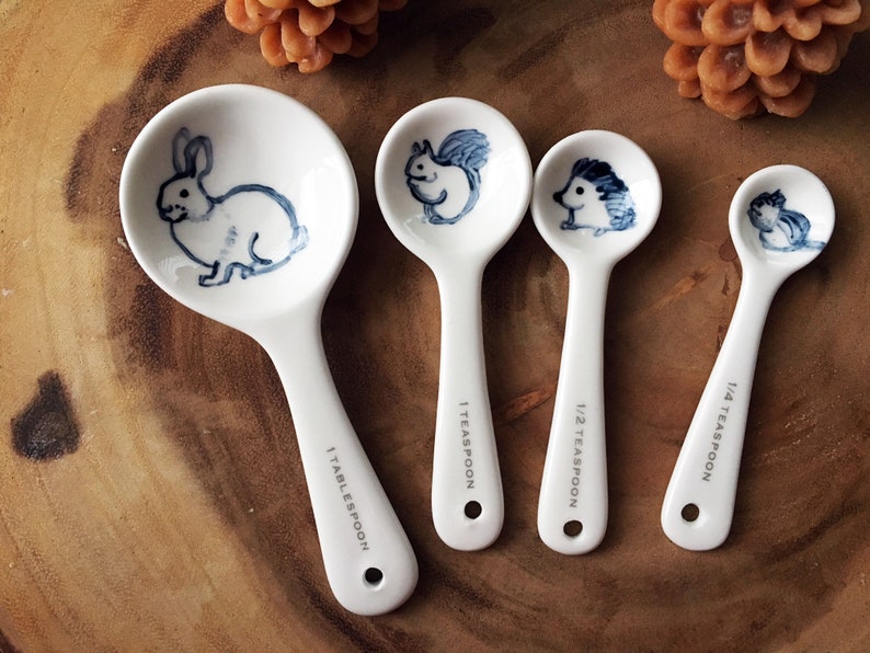 Puede incluir: Conjunto de cuatro cucharas medidoras de cer&aacute;mica blanca con ilustraciones de animales azules. Las cucharas est&aacute;n etiquetadas como 1 cucharada, 1 cucharadita, 1/2 cucharadita y 1/4 cucharadita.
