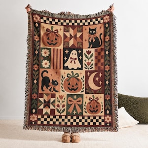 Könnte beinhalten: Eine gewebte Wohndecke mit Patchwork-Design und Halloween-Motiven wie Kürbissen, einer schwarzen Katze mit Schleife, einem Geist, einer Mondsichel, Sternen und Blumenmustern. Die Decke hat einen Fransenrand und eine karierte Bordüre.