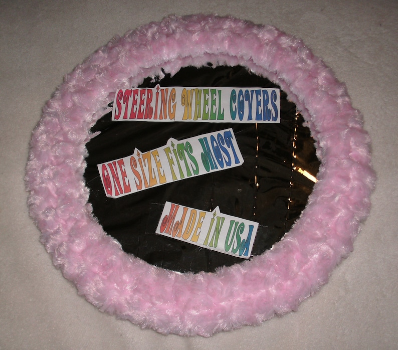 Puede incluir: Funda de volante de color rosa peludo con texto arco&iacute;ris que dice "Steering Wheel Covers", "One Size Fits Most" y "Made in USA".
