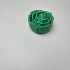 May include: A green, multi-layered, spherical object resembling a head of lettuce or cabbage. The item is constructed from several concentric, nested segments that fit together to form a rounded, textured shape with ruffled edges.