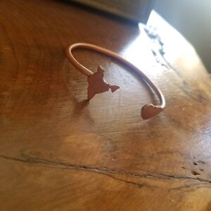 May include: A copper-colored bracelet with a heart-shaped charm and a cutout of the shape of India.