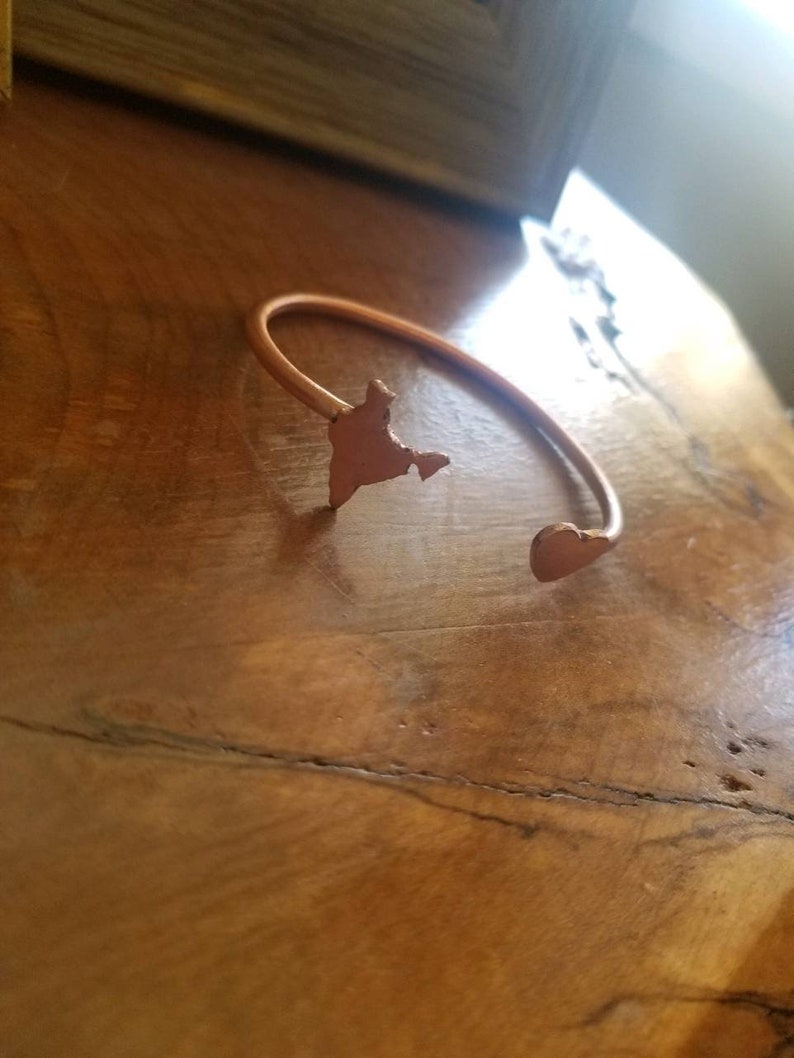 May include: A copper-colored bracelet with a heart-shaped charm and a cutout of the shape of India.