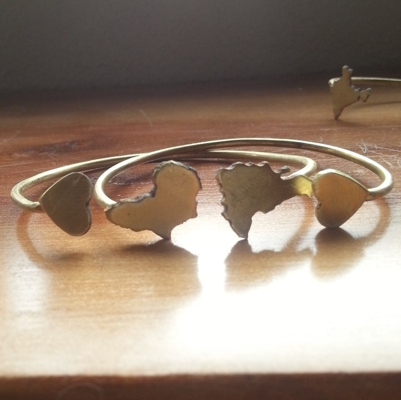 May include: Three gold-toned metal bracelets with heart-shaped cutouts. The bracelets are stacked on top of each other.