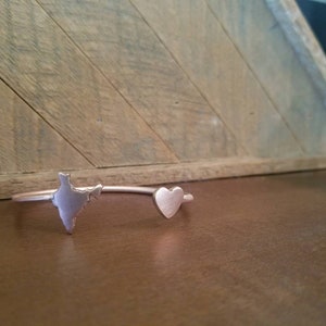 May include: A silver bracelet with a heart and an outline of India. The bracelet is on a wooden surface.