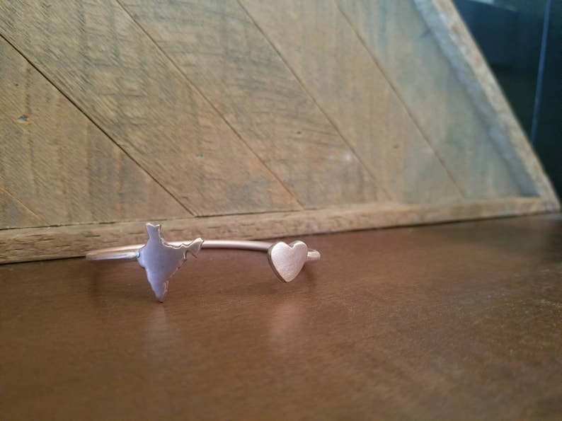 May include: A silver bracelet with a heart and an outline of India. The bracelet is on a wooden surface.