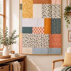 Puede incluir: Una colcha de pared rectangular con un diseño de patchwork de varios patrones de tela en tonos amarillo mostaza, naranja quemado, verde salvia, blanco y azul claro, con un borde amarillo mostaza y colgada de una barra de madera.