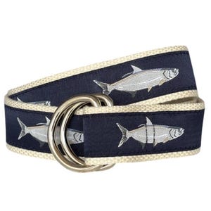 May include: A navy blue belt with a white border and a silver buckle. The belt is decorated with a repeating pattern of silver tarpon fish.