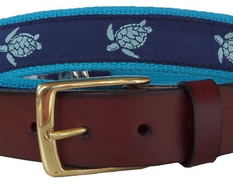 May include: A brown leather belt with a gold buckle and a blue and turquoise patterned fabric strap with white sea turtle designs.