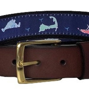 May include: A brown leather belt with a blue and white patterned fabric strap. The strap features a repeated design of a stylized island with pink, blue, and white accents. The belt buckle is gold-toned.