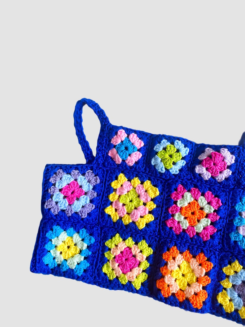 May include: A blue crochet top with colorful granny squares. The top has two straps and is made with a variety of bright colors, including pink, yellow, green, and orange.