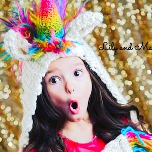 May include: A white crocheted unicorn hat with a rainbow horn and colorful feather accents. The hat is worn by a person with dark hair and a surprised expression. The text "Lily and Mason" is written in cursive.