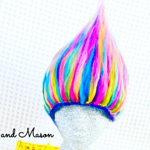 Op de afbeelding: Een kleurrijke, veelkleurige, regenboogkleurige trollenpruik gemaakt van garen. De pruik zit op een wit mannequinhoofd.