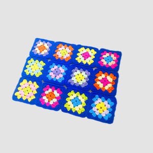 May include: A blue crocheted blanket with colorful squares. Each square has a different pattern of pink, yellow, orange, blue, and green.