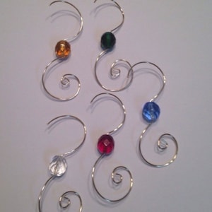 May include: Five silver wire ornament hooks with colorful glass beads. The beads are orange, green, blue, red, and clear.