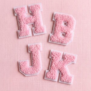 May include: Four individual letter patches featuring the letters H, B, J, and K. Each letter is crafted from a textured, light pink chenille fabric with a soft, fuzzy appearance, outlined by a white felt border for a clean, defined edge.