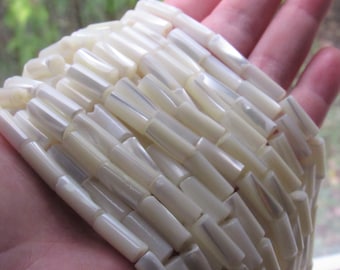 May include: A strand of white iridescent shell beads, each bead is a long cylinder shape.