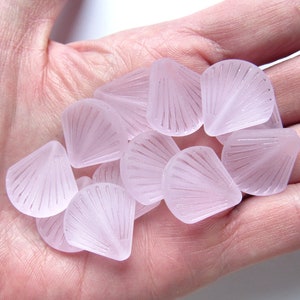 May include: A group of pale pink glass beads with a fan-shaped design. The beads are translucent and have a frosted finish.
