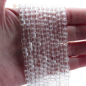 May include: A strand of clear glass beads, each bead is a square shape with a faceted design.