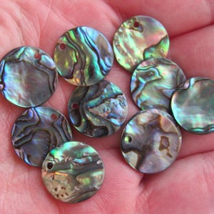 May include: A collection of iridescent abalone shell pendants. Each round pendant has a unique pattern of blues, greens, and purples, with a small hole for stringing. The pendants are ideal for jewelry making or craft projects.