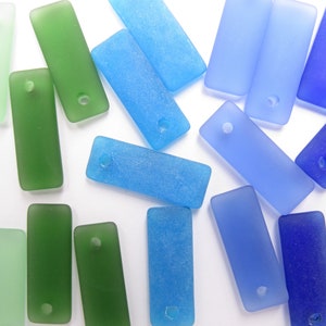 May include: Assortment of frosted glass rectangular beads in shades of blue, green, and light green. Each bead has a small hole for stringing.