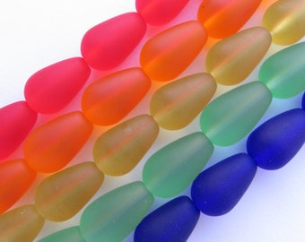 May include: A strand of frosted glass beads in a rainbow of colors, including pink, orange, yellow, green, blue, and purple. The beads are oval shaped and have a smooth, matte finish.