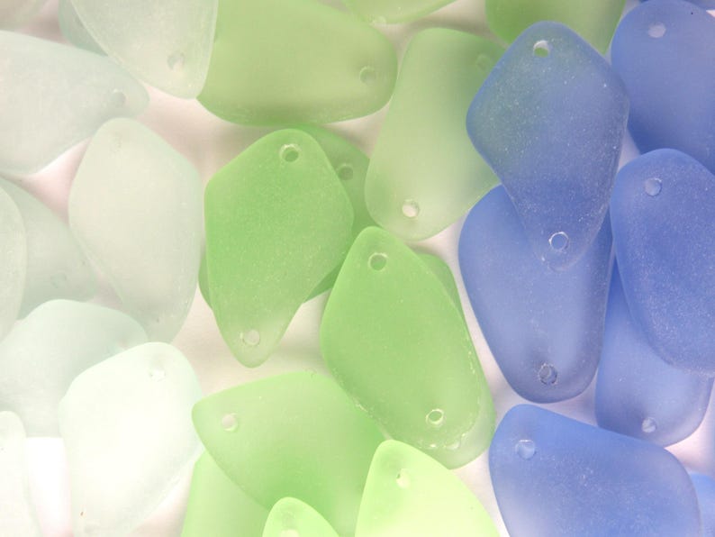 May include: Assortment of sea glass pieces in various shades of blue, green, and white. The sea glass is smooth and translucent, with a frosted finish.