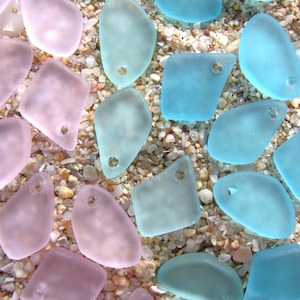 May include: A collection of frosted, translucent glass pendants in shades of soft pink and light blue. Each piece features an irregular, organic shape with a single pre-drilled hole near the top edge, suitable for use as jewelry components.