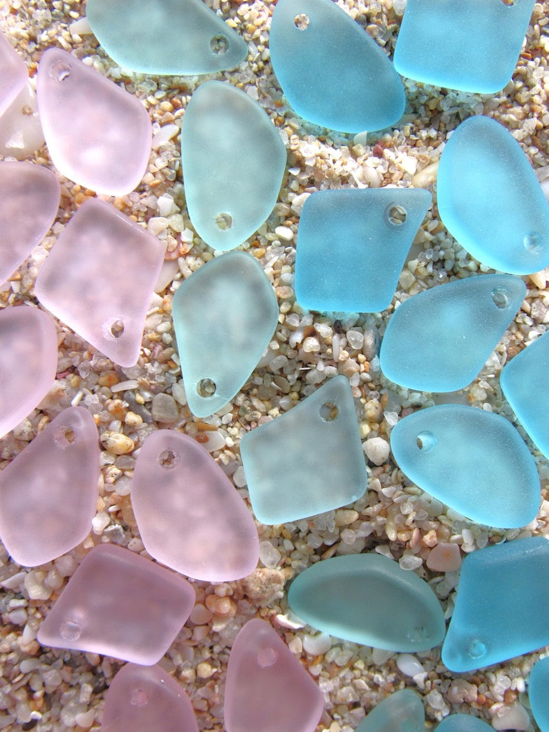 May include: A collection of frosted, translucent glass pendants in shades of soft pink and light blue. Each piece features an irregular, organic shape with a single pre-drilled hole near the top edge, suitable for use as jewelry components.