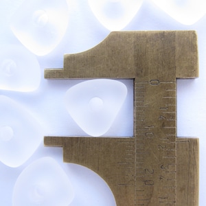 以下が含まれることがあります： 透明なガラスの三角形を測定する金属製のノギスのクローズアップ。ノギスは三角形を約3.8cmの幅で測定しています。