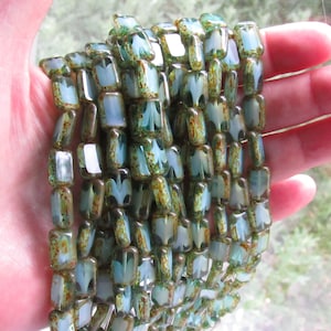 May include: A strand of green and brown glass beads with a white floral pattern. The beads are rectangular and have a slightly iridescent finish.