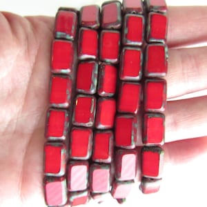 May include: A strand of red square ceramic beads with a metallic finish. The beads have a slightly uneven surface and are strung together on a clear thread.