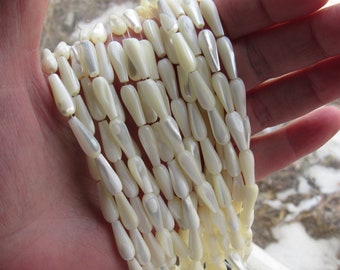 May include: A strand of white mother of pearl teardrop beads. The beads are smooth and have a slight iridescent sheen.