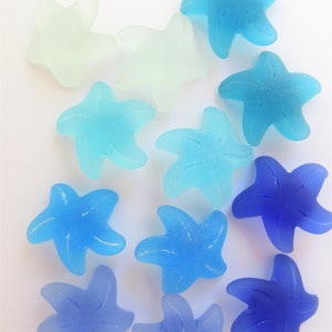 May include: A collection of twelve starfish-shaped beads in a gradient of colors, ranging from translucent pale white and light aqua to vibrant sky blue and deep royal blue. Each bead features a smooth, frosted finish and a five-pointed design.