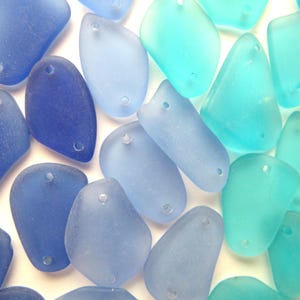 May include: A collection of sea glass beads in shades of blue and turquoise. The beads are smooth and have a frosted finish. They have two holes each for stringing.