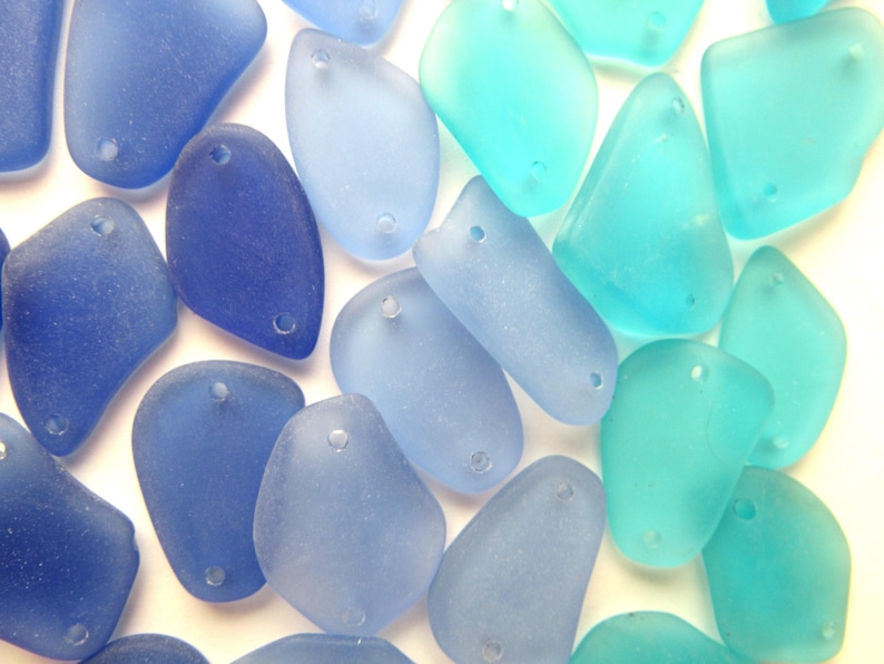 May include: A collection of sea glass beads in shades of blue and turquoise. The beads are smooth and have a frosted finish. They have two holes each for stringing.