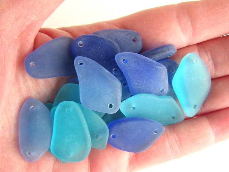 May include: A collection of sea glass charms in shades of blue and turquoise. Each charm has two holes for attaching to jewelry or other crafts.