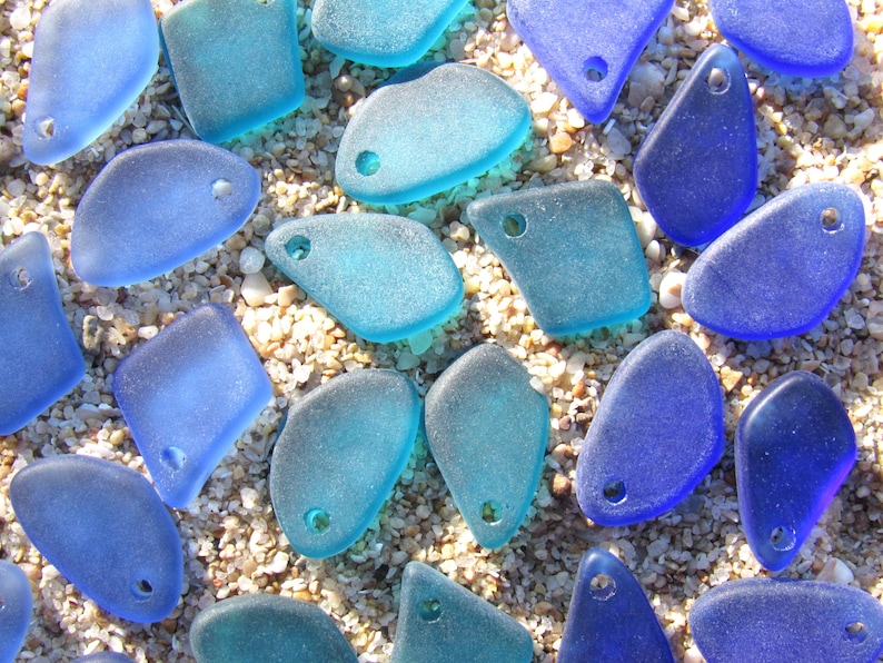 May include: A collection of assorted sea glass pieces in various shades of blue and turquoise. Each piece features a smooth, frosted texture and a single pre-drilled hole, making them ready for use as individual jewelry components or charms.