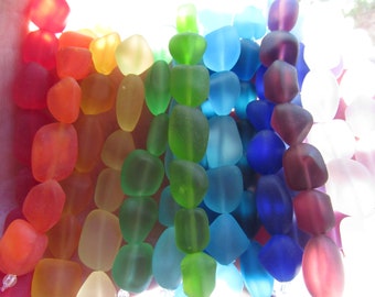 May include: A vibrant rainbow of sea glass beads strung together. The beads transition from red to orange, yellow, green, blue, and purple. Each bead has a unique shape and frosted texture, creating a colorful and eye-catching display.