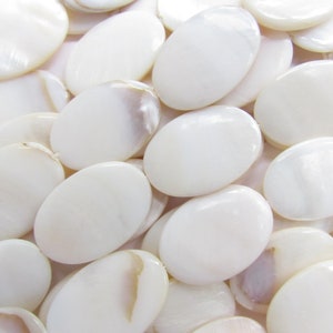 May include: A close-up of a pile of white oval-shaped mother of pearl beads. The beads have a smooth, glossy finish and are perfect for jewelry making.
