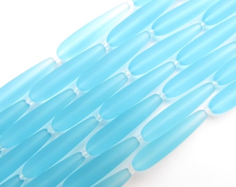 May include: A strand of light blue glass beads, each bead is long and narrow, resembling a teardrop shape.