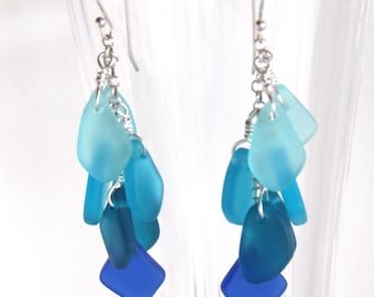 May include: A pair of dangle earrings with a gradient of blue glass beads. The earrings are made with silver wire and have a hook closure.