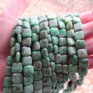 May include: A strand of square-shaped green gemstone beads. The beads have a mottled, marbled appearance.