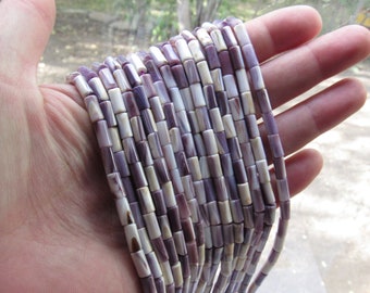 May include: A strand of purple and white shell beads. The beads are cylindrical and have a natural, organic look.