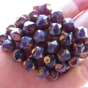 Puede incluir: Un grupo de cuentas facetadas en tonos azul profundo y bronce. Las cuentas tienen una forma geométrica y un brillo metálico, creando una apariencia texturizada. Las cuentas están agrupadas.