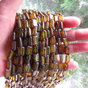 May include: A strand of iridescent amber glass beads, each bead is rectangular and has a slightly irregular shape.