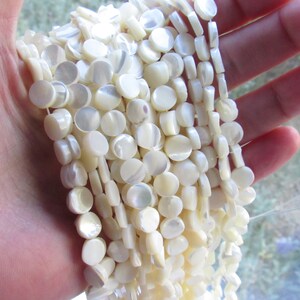 May include: A strand of white mother of pearl beads. The beads are round and flat, with a slightly iridescent finish.