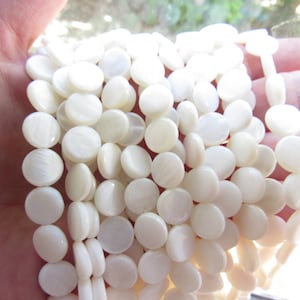 May include: A strand of white mother of pearl beads. The beads are round and flat, and they have a slightly iridescent sheen.